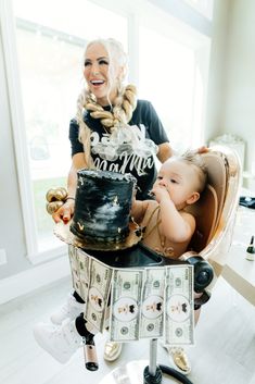 a woman holding a baby in front of a birthday cake with money on the table