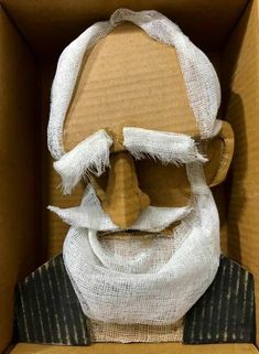 a cardboard box that has a doll in it with a white beard and headdress