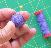 a hand holding a purple ball of thread next to a spool of thread