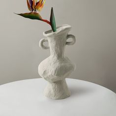 a vase with a flower sticking out of it on a white table next to a gray wall