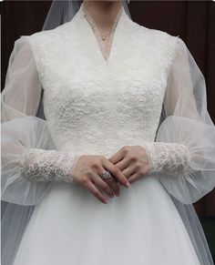 a woman wearing a wedding dress and veil with her hands on her chest, standing in front of a wooden wall