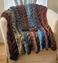 a couch with a blanket on top of it in front of a window and a chair