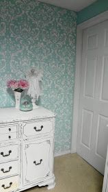 a white dresser with flowers in a vase on it's top and wallpaper