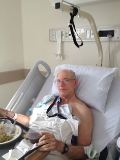 an older man laying in a hospital bed with food on the tray and his arm around him