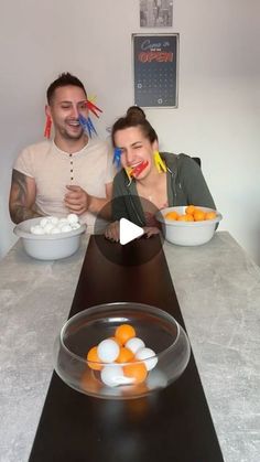 two people sitting at a table with oranges and marshmallows in bowls