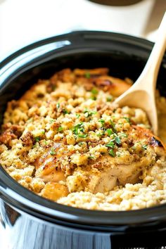 a crock pot filled with chicken and rice next to a wooden spoon on a table