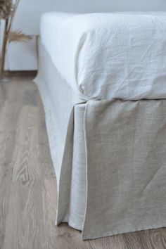 a bed with white sheets and wooden flooring next to a vase filled with flowers