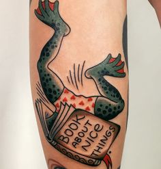 a person with tattoos on their legs has a frog reading a book and holding an open book