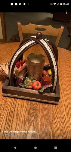 a wooden table topped with a candle holder filled with fall leaves and pumpkins on top of it