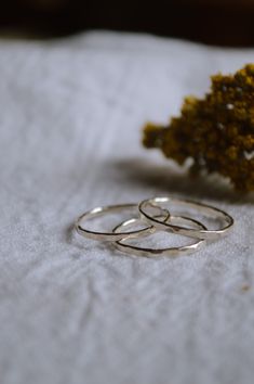 two silver rings sitting on top of a white towel next to a yellow flower in front of it