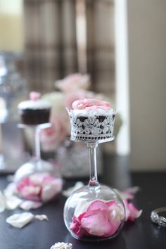 some pink flowers are in a glass vase on a table with other small cups and spoons