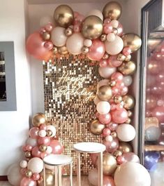 a room filled with balloons and tables next to a wall covered in gold, white and pink