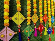 many colorful kites are hanging on a wall with grass and flowers around them,