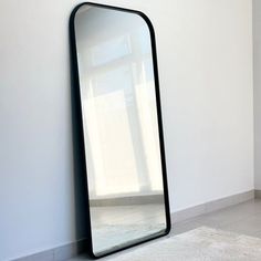 a large black mirror on the wall next to a white rug in a room with light coming through it