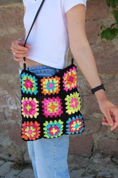 a woman holding onto a crocheted bag with flowers on the front and sides