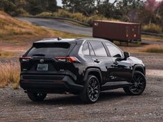 the rear end of a black toyota rav parked on a gravel road in front of a trailer