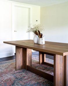 a wooden table sitting on top of a rug next to a vase filled with flowers