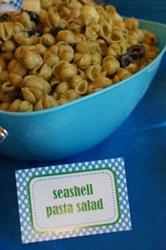 a blue bowl filled with pasta on top of a table next to a sign that says seashell pasta salad