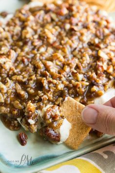 a person holding a piece of bread with nuts and cream on it in front of some crackers