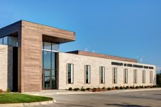 the front of a building with large windows and grass on the side of the street