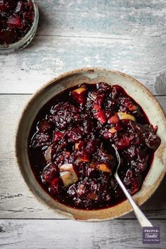 a bowl filled with cranberry fruit and apple chutney on top of a white wooden table