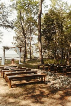 an outdoor ceremony setup with wooden benches and white drapes on the top of them