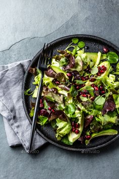 a black plate topped with lettuce and pomegranates next to a fork