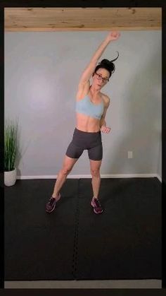 a woman standing on top of a black mat with her arms in the air and one leg up