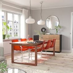 a dining room table with orange chairs and a laptop on it, in front of a large window