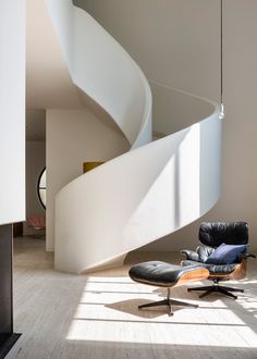 a modern chair and ottoman in front of a spiral staircase with light coming through the window