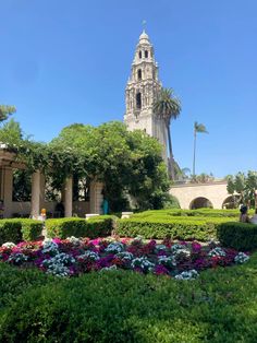 a clock tower towering over a lush green park filled with lots of flowers and trees