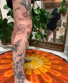 a person with tattoos on their legs standing in front of a mirror and flower rug