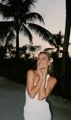 a woman standing in front of palm trees with her hands on her face and smiling