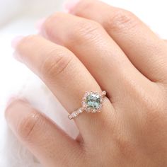 This artfully sculpted green sapphire engagement ring features a 6x6mm cushion cut conflict free cultured seafoam green sapphire in our signature vintage floral diamond and finished in the diamond scalloped band to complete its distinctive and elegant look. Adore your future bride with this vintage halo diamond sapphire ring. It can be made in your choice of platinum or 18k or 14k yellow, rose, or white gold. A matching bridal ring set is available.** The listing price is for one engagement ring Fine Jewelry Green Sapphire Ring With Rose Cut Diamonds, Green Sapphire Ring With Rose Cut Diamonds, Green Diamond Ring With Rose Cut, Green Sapphire Rings With Halo Setting, Green Sapphire Diamond Ring With Round Cut, Green Rose Cut Diamond Wedding Jewelry, Green Sapphire Diamond Ring For Promise, Green Sapphire Diamond Promise Ring, Green Sapphire Ring With Halo Setting For Promise