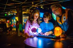 two children and an adult looking at a tablet computer in a dark room with other people