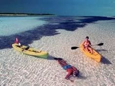 two people in kayaks paddling on the beach with one person upside down and another standing up