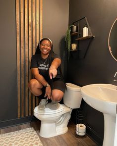 a woman sitting on top of a white toilet in a bathroom next to a sink