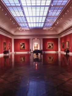 an empty room with red walls and paintings on the wall, in front of a skylight