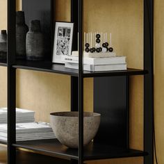 a black book shelf with books and vases on it, next to a bowl