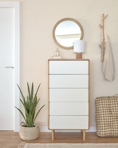 a white dresser sitting next to a potted plant on top of a wooden floor