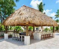 an outdoor kitchen with a thatched roof and bar seating area next to the pool