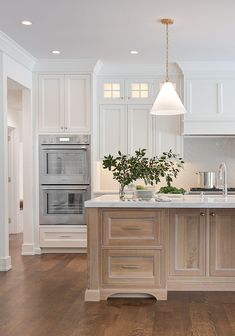 a large kitchen with white cabinets and wood flooring is pictured in this image, there are two ovens on the island