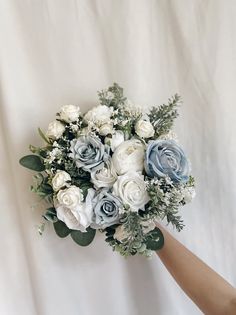 a bouquet of white and blue flowers is being held by a person's hand