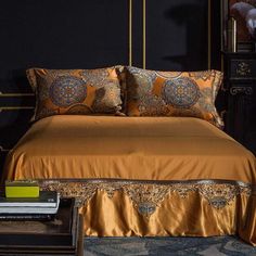 a bed with gold sheets and pillows on top of it next to a night stand