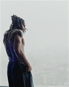 a man with dreadlocks standing in front of a window looking at the city