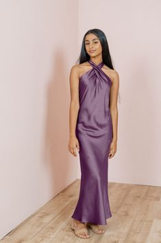 a woman in a purple dress standing on a wooden floor with her hands behind her back