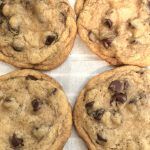 four chocolate chip cookies sitting on top of a piece of parchment paper