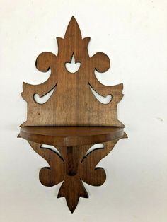 a wooden shelf with an ornate design on the top and bottom part, hanging from a white wall