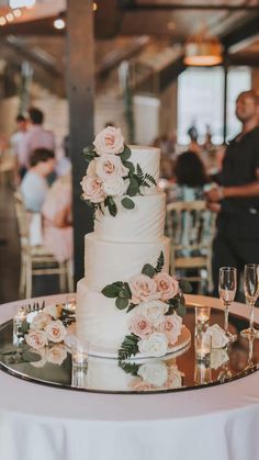 a white wedding cake with pink flowers and greenery sits on top of a round table