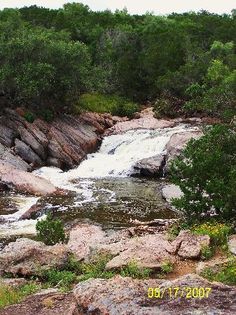 there is a small waterfall in the middle of this rocky area with trees around it